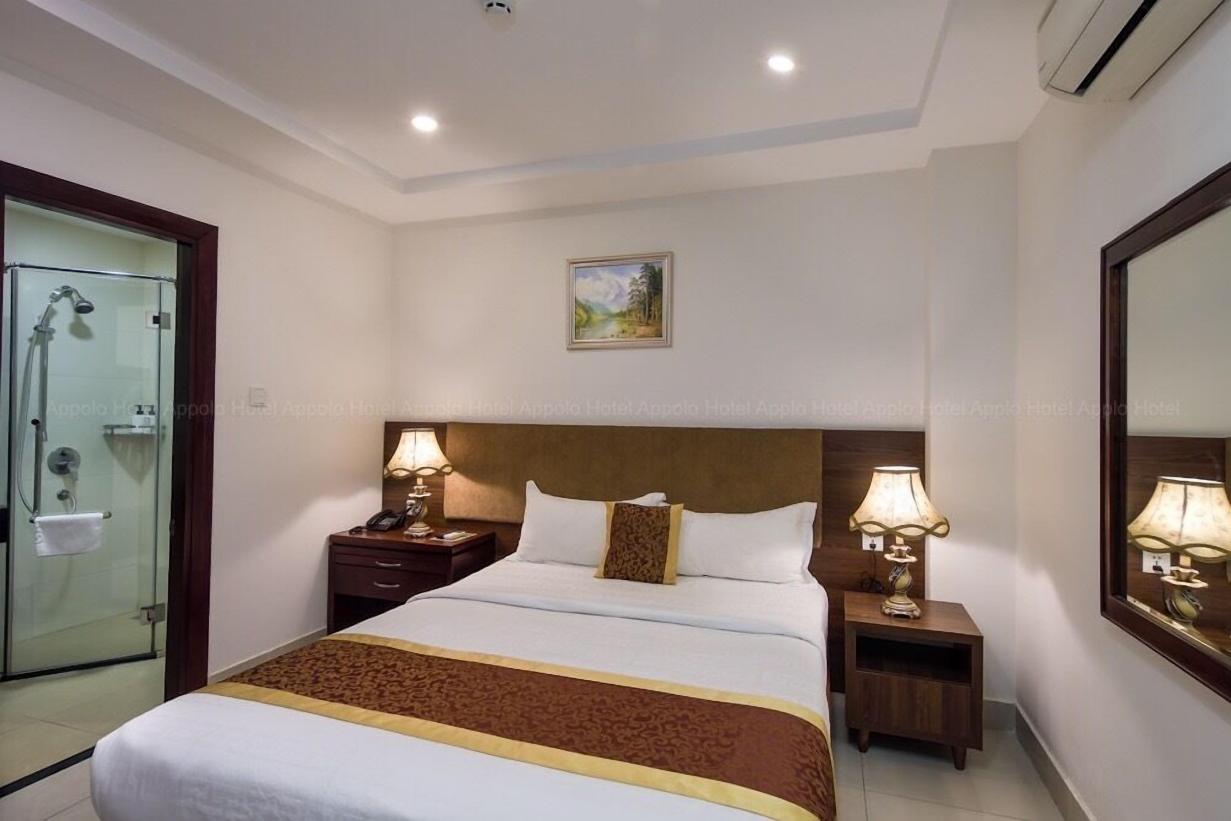Une chambre d’hôtel avec un grand lit, deux tables de chevet avec des lampes, une cabine de douche en verre et un tableau au mur.