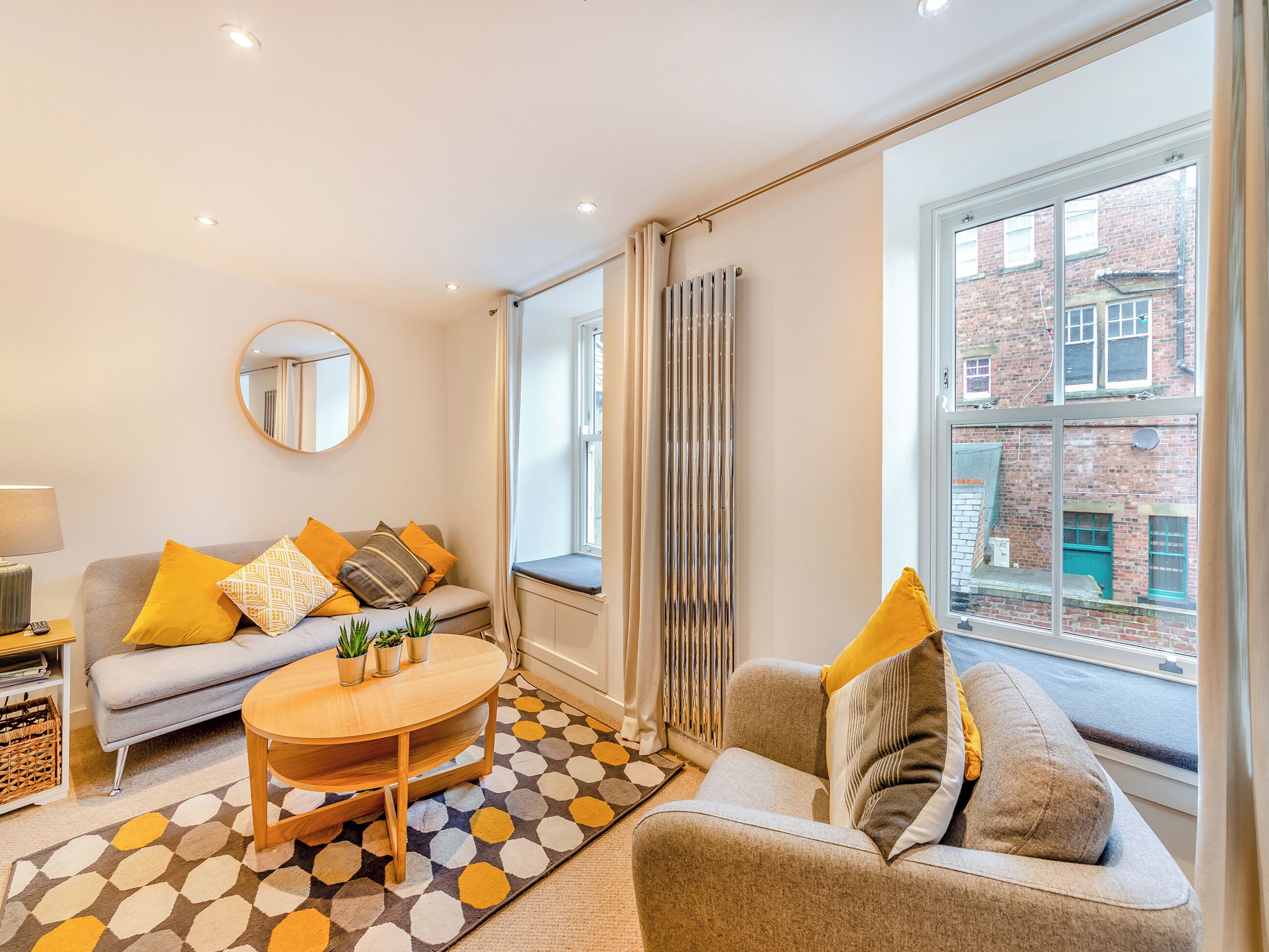 A modern living room with a sofa, a round coffee table, and a large window with a view of a brick building.