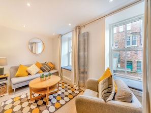A modern living room with a sofa, a round coffee table, and a large window with a view of a brick building. - Town Square House - UK45610 (Alnwick)