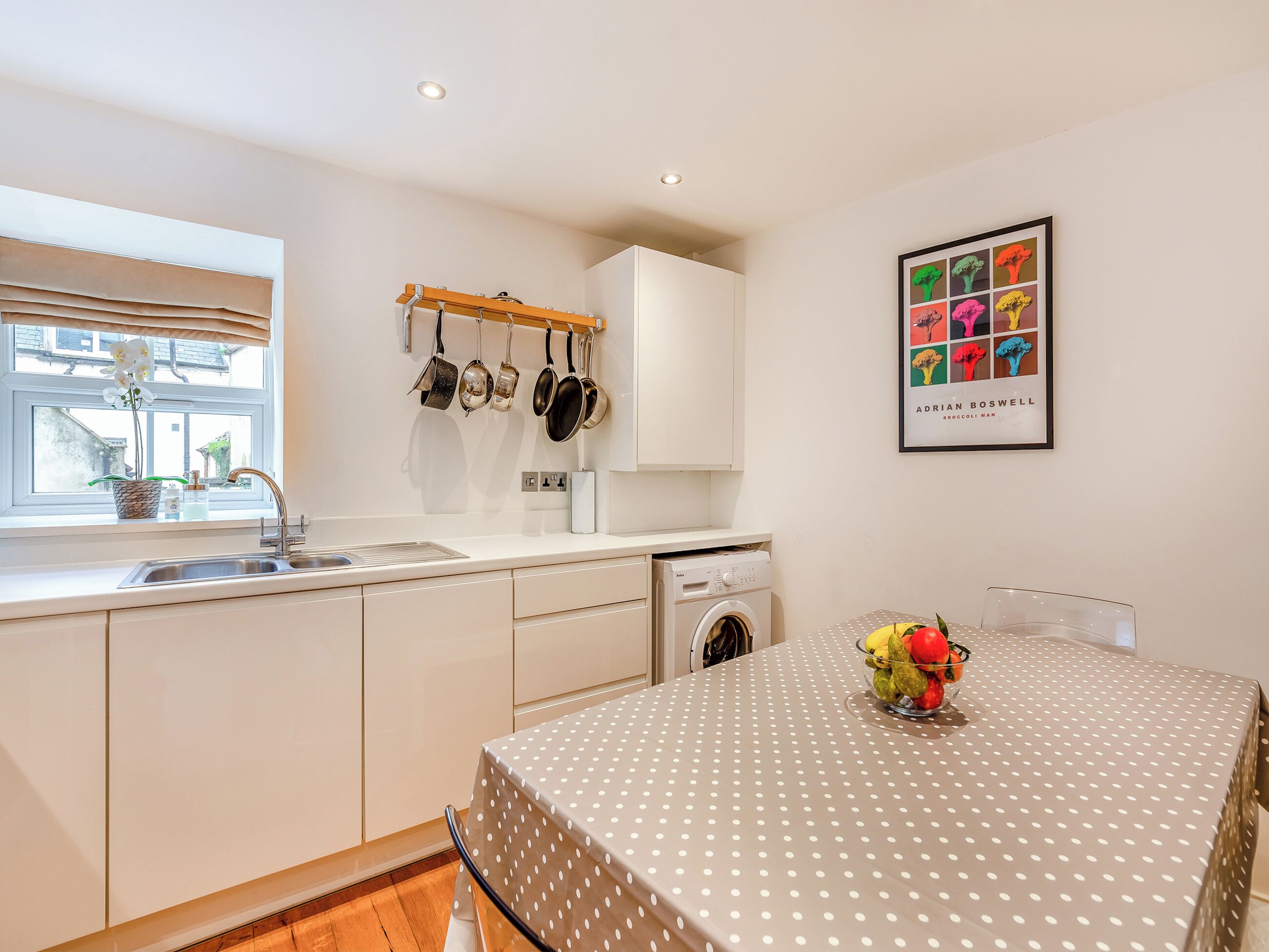 A kitchen with a washing machine, a sink, and a dining area with a polka-dotted tablecloth.