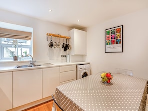 A kitchen with a washing machine, a sink, and a dining area with a polka-dotted tablecloth. - Town Square House - UK45610 (Alnwick)