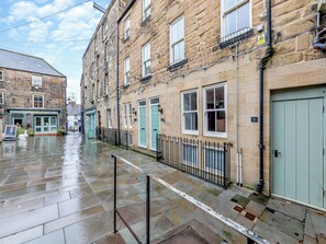 A street with stone buildings, a wet pavement, and a metal fence. - Town Square House - UK45610 (Alnwick)