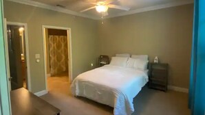 Ein Schlafzimmer mit einem Bett, einem Nachttisch, einem Deckenventilator und einer Tür zu einem weiteren Raum.