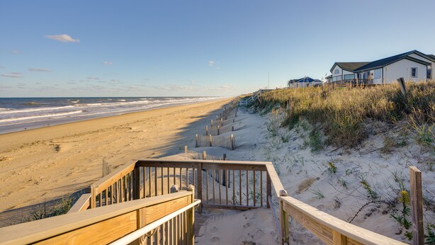 A beach with wooden walkways leading to a white building with a dark roof.