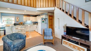 A spacious living area with a high ceiling, wooden staircase, and a modern kitchen in the background.