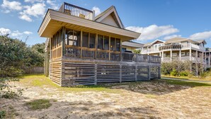 A beachfront house with a large balcony, multiple levels, and a wooden deck.
