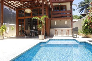 A pool area with a tiled deck, a pergola, and a bar area with stools and a grill. - Casa Itacaré - Santa Onda (Itacaré)