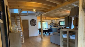 Une cuisine spacieuse avec des poutres apparentes, un coin repas doté d’une table ronde et un escalier menant à un niveau supérieur.