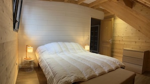 Une chambre confortable avec un lit, des lampes de chevet, une armoire en bois et un plafond en pente.