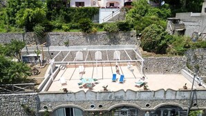 Eine Dachterrasse mit Liegestühlen, einem kleinen Pool und einer Steinsäule.