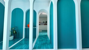Ein modernes Interieur mit türkisfarbenen Wänden und weißen Bögen, durch die eine Küchenzeile sichtbar ist, sowie ein gemustertes Parkett.