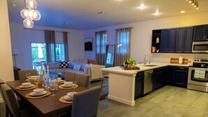A modern kitchen with dark cabinets, a central island, and a dining area with a table set for four. - BaeCation Dania! Near Fort Lauderdale Airport, beach & casino!
pool & jacuzzi! (Dania Beach)