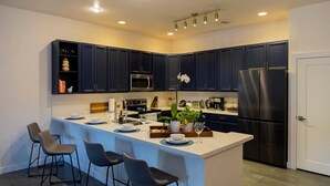 A modern kitchen with dark blue cabinets, a stainless steel refrigerator, and a central island with bar stools. - BaeCation Dania! Near Fort Lauderdale Airport, beach & casino!
pool & jacuzzi! (Dania Beach)