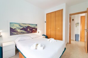 Habitación de hotel con cama, armario de madera, mesita de noche, un cuadro colgado en la pared de montañas y un baño visible a través de una puerta abierta.