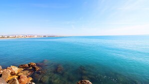 Vista sulla costa con acque blu cristalline, un litorale roccioso e edifici in lontananza.