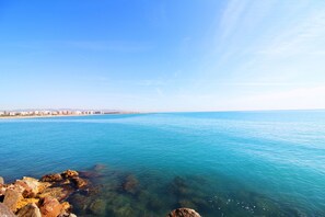 Une vue sur la côte, avec une eau d’un bleu limpide, un rivage rocheux et une silhouette de ville qui se dessine à l’horizon.