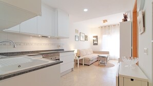Una cucina moderna con mobili bianchi, un lavello e un piano di lavoro. C'è una zona pranzo con tavolo e sedie, e un divano.