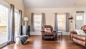 A living room with a brown leather sofa, a recliner with a reindeer pillow, a small table, and a lamp. - Parkwood Manor at Bear Creek Lakes in Jim Thorpe (Jim Thorpe)
