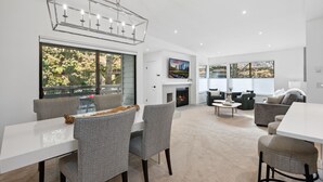 Un salon moderne avec une cheminée, un coin repas avec une table et des chaises, et une grande fenêtre donnant sur la forêt.