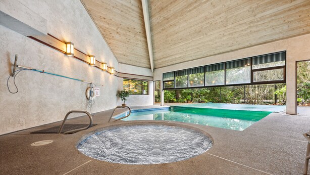 Une piscine intérieure dotée d’un jacuzzi, d’un plafond en bois et de grandes fenêtres.