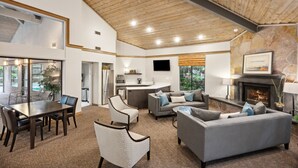 Un vaste espace de vie doté d’un haut plafond, d’une cheminée, d’un coin repas avec une table et des chaises, et d’une cuisine située à l’arrière-plan.