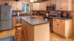 A modern kitchen with wooden cabinets, stainless steel appliances, and a central island with stools. - Scootberry Cabin, Peaceful Log Home Perfect for the Family (Seward)