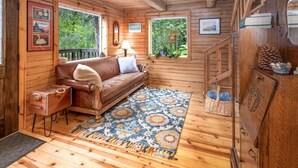 A cozy cabin interior with a wooden floor, a leather sofa, a patterned rug, and a small side table. - Scootberry Cabin, Peaceful Log Home Perfect for the Family (Seward)