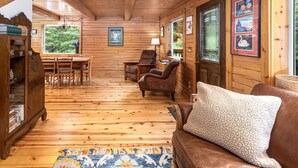 A wooden cabin interior with a dining area, a sofa, and a rug. - Scootberry Cabin, Peaceful Log Home Perfect for the Family (Seward)