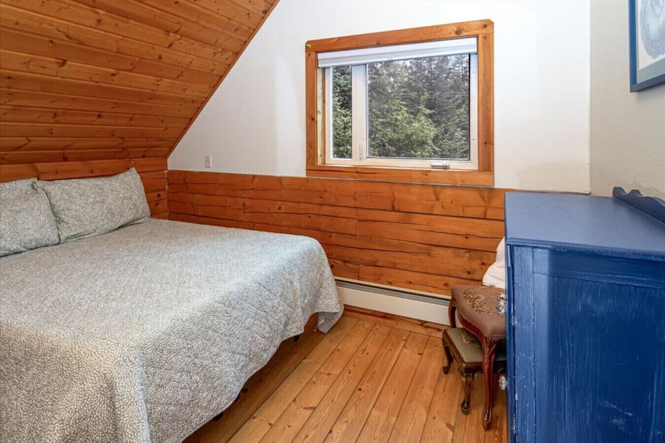 A bedroom with a sloped ceiling, a bed, a window, and a dresser.
