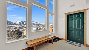 Ett rum med stora fönster som ger utsikt över bergen, en träbänk och en grön dörr.