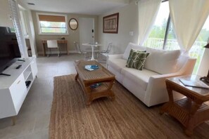 Una sala de estar con un sofá blanco, una mesa de centro, un televisor y un comedor con una mesa y sillas.
