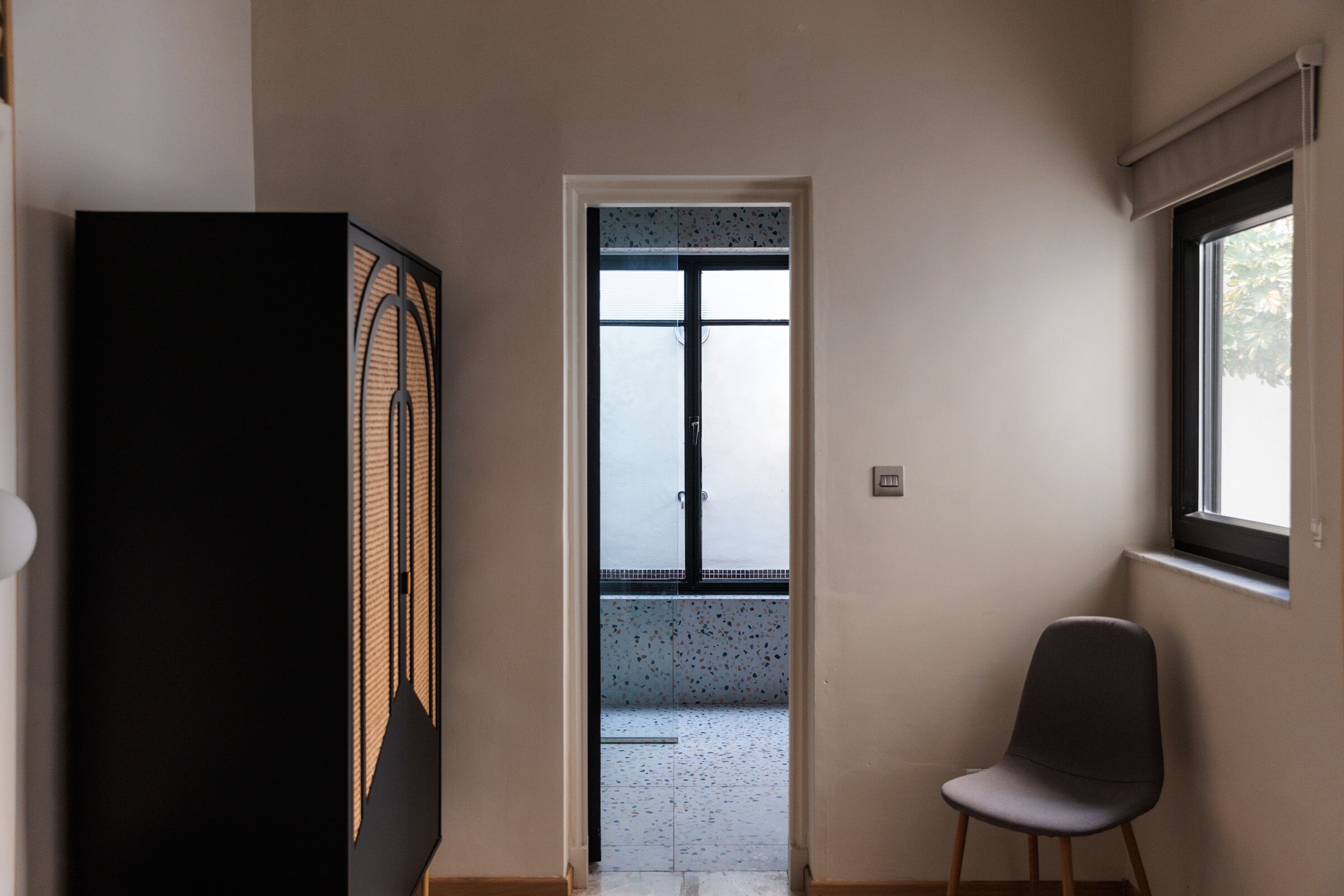 A hallway with a door leading to a balcony, a chair, and a black cabinet.