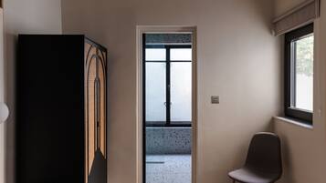 A hallway with a door leading to a balcony, a chair, and a black cabinet.