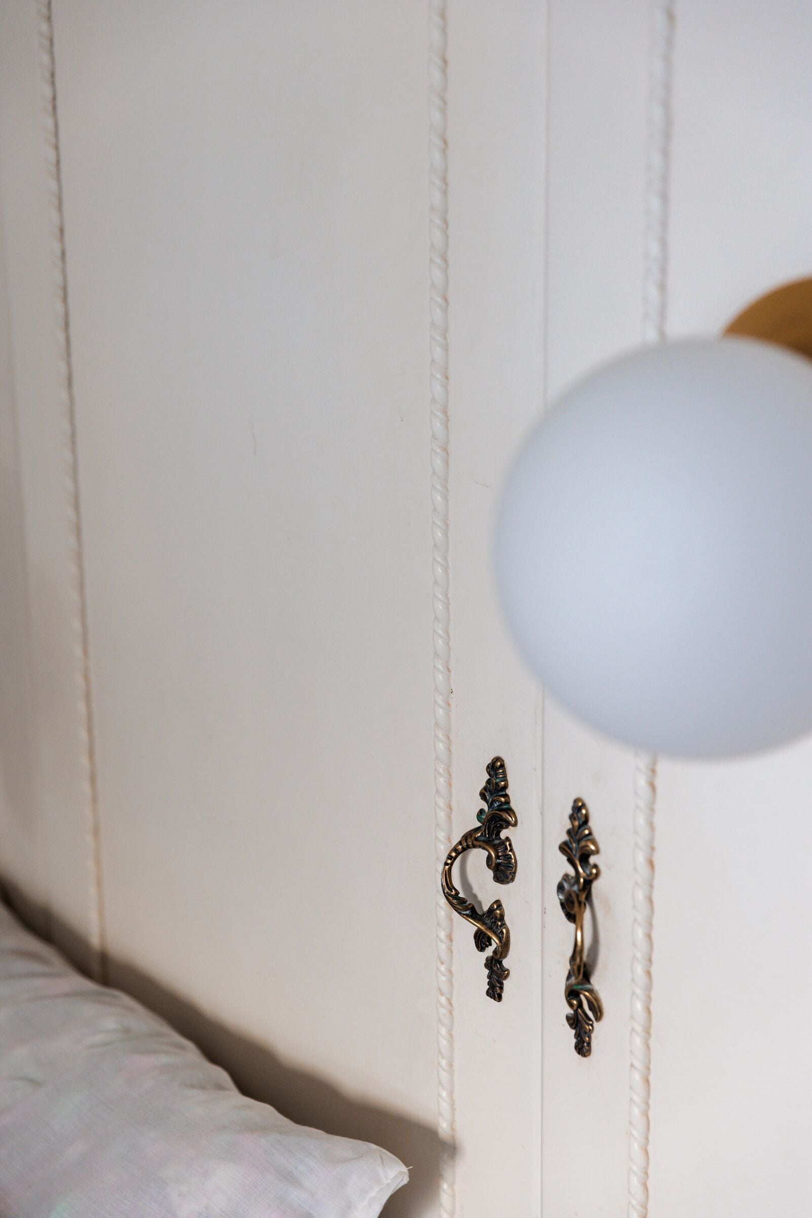 A white wardrobe with ornate metal handles and a white lamp.