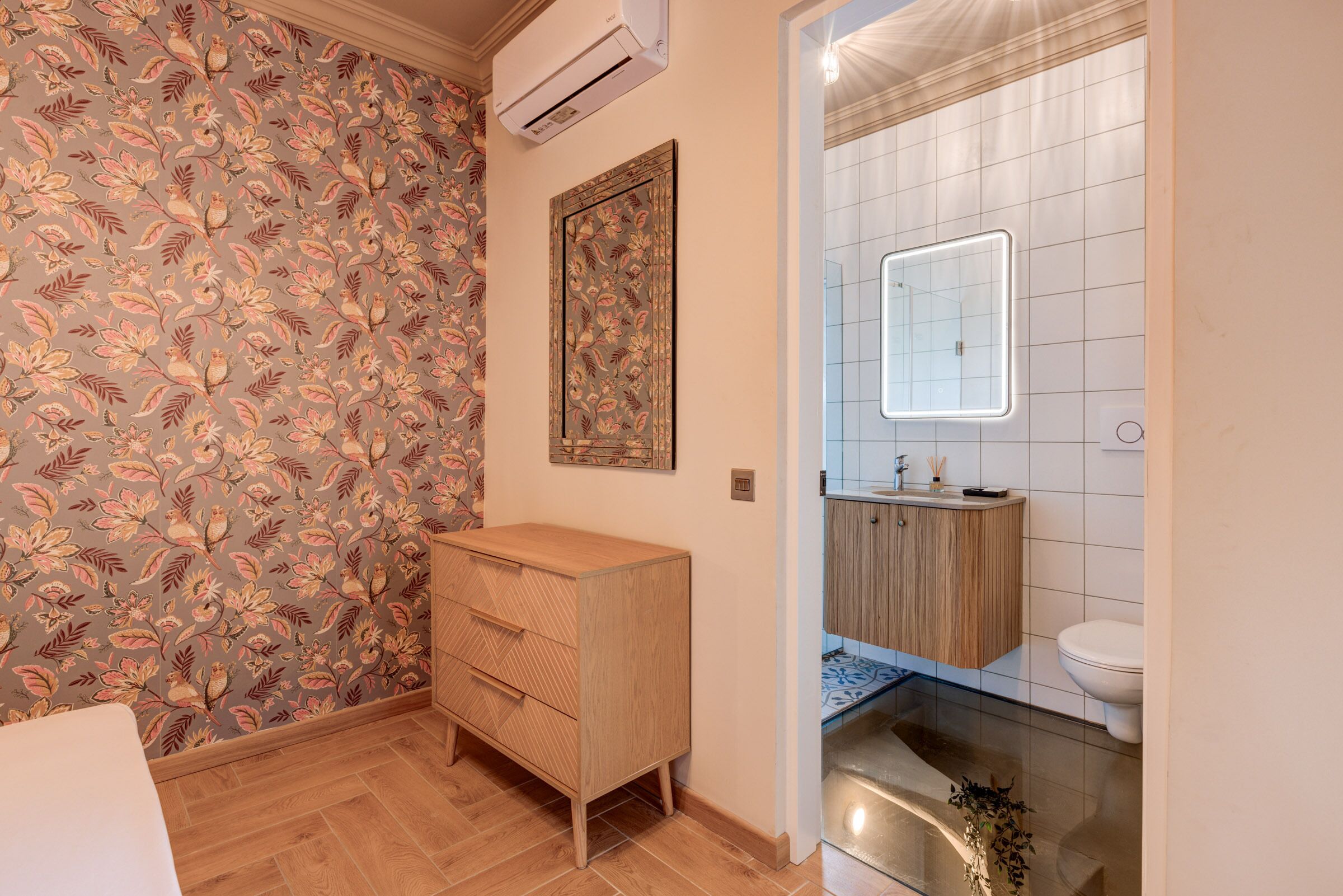 Ein Badezimmer mit weiß gefliesten Wänden, einem Holzschrank, einem Spiegel mit Beleuchtung und einer Toilette.