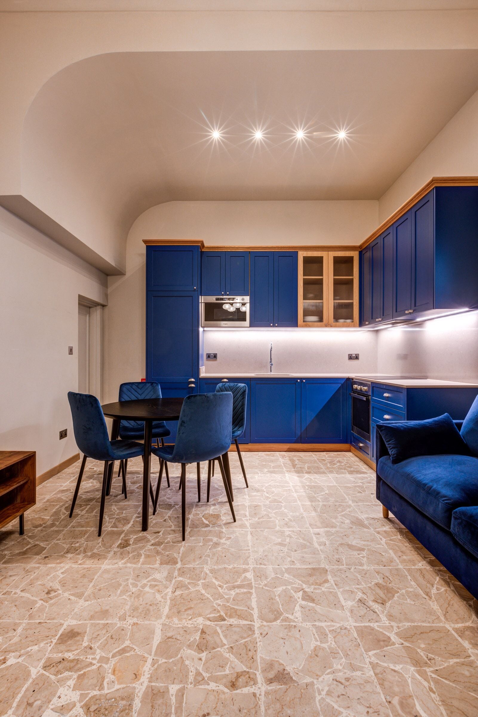 Une cuisine de taille réduite avec des meubles bleus, une table à manger avec des chaises et un canapé bleu.