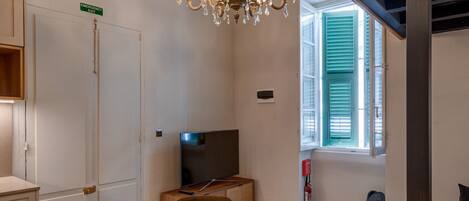 A dining area with a wooden table and chairs, a chandelier, and a television in the background.