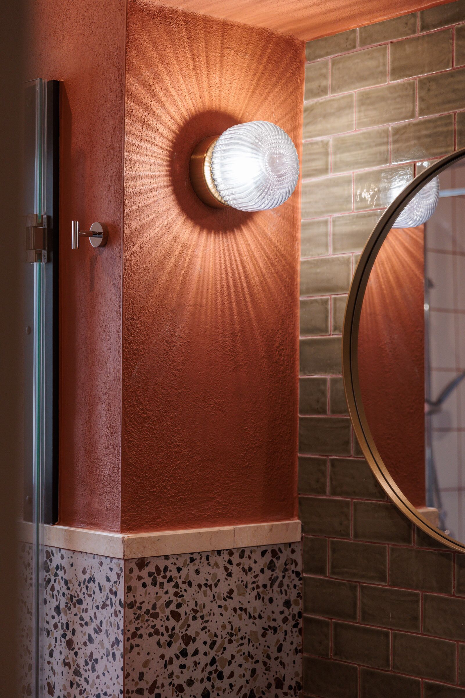 A bathroom with a textured wall, a round mirror, and a door with a metallic handle.