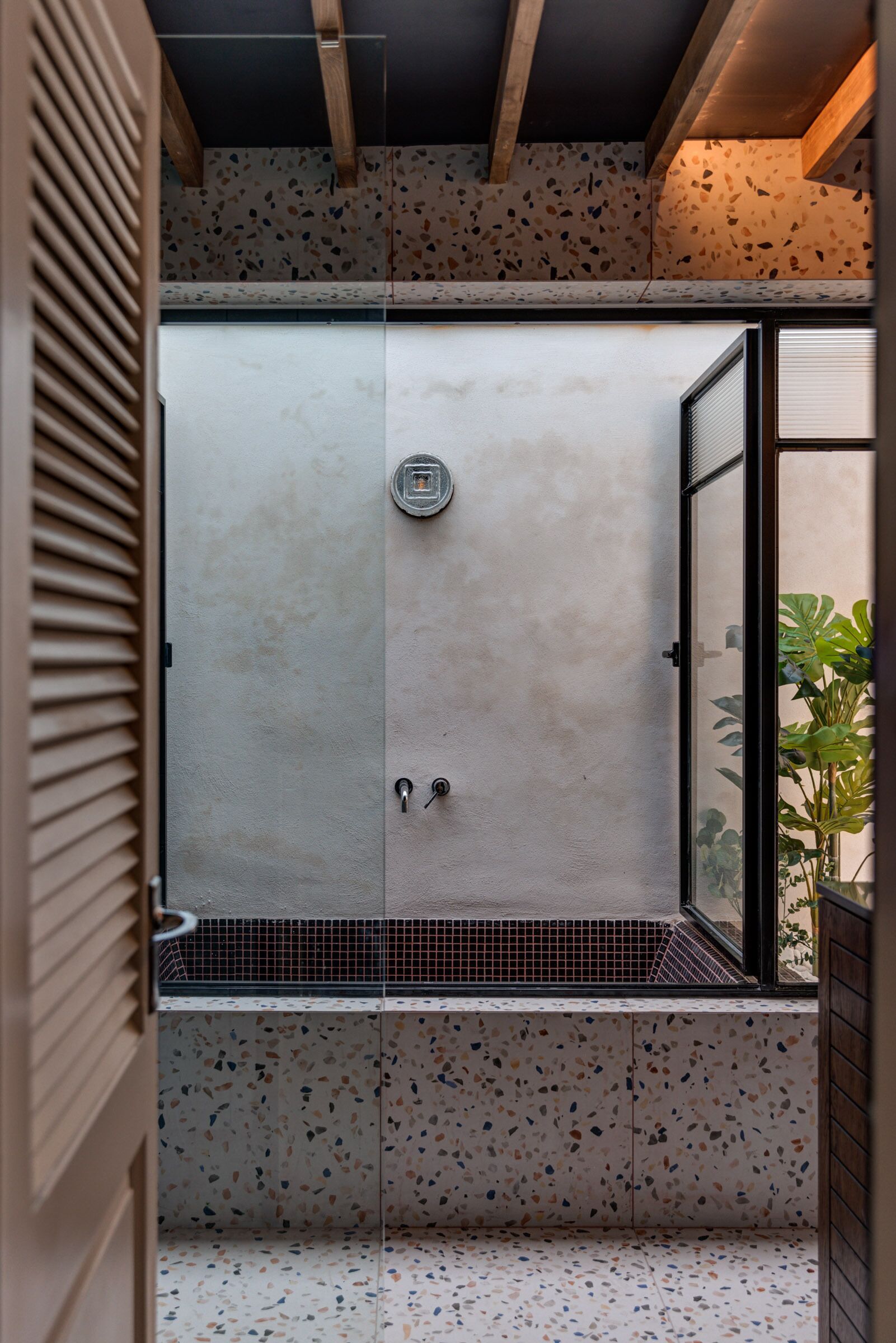 A modern shower with a glass door, a metal shower head, and a speckled tile floor.