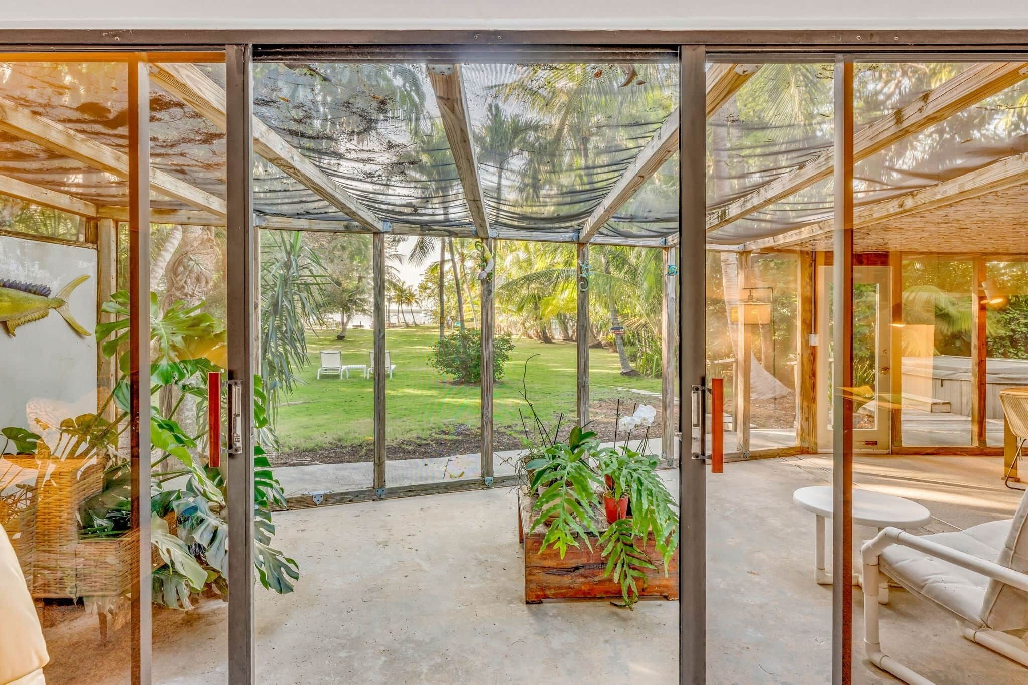 Une chambre moderne avec une porte vitrée donnant sur un jardin. À l’intérieur, on trouve une table et des chaises en bois, ainsi qu’une plante en pot.