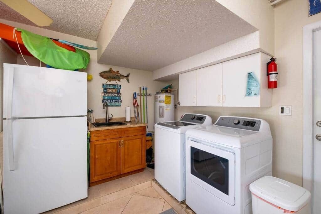 Una cocina compacta con refrigerador, lavadoras, gabinetes de madera y extintor.
