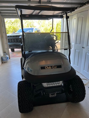 En golfbil med en etikett som visar att den är av märket ”Club Car”, parkerad i ett garage.
