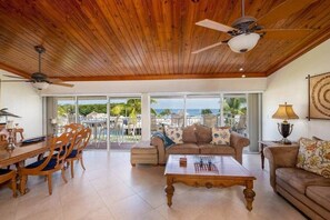 Ein geräumiges Wohnzimmer mit Holzbalkendecke, Deckenventilator, einer Couch, einem Couchtisch und einem Essbereich mit Stühlen und einem Tisch.
