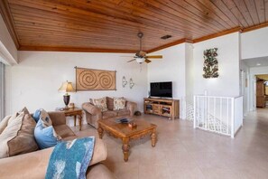 Ein Wohnzimmer mit Holzboden, Deckenventilator, Fernseher, Sofa, Couchtisch und einer Treppe mit Geländer.