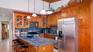 A kitchen with wooden cabinets, a stainless steel refrigerator, a granite countertop, and pendant lights. - Oceanview Marinaview Free Golf Cart Pool Pickleball (Key Largo)