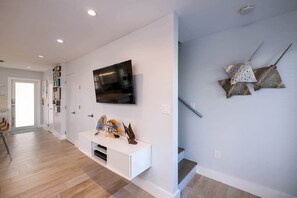 Um interior moderno com televisão de tela plana na parede, um console branco com objetos decorativos e uma escada com uma peça de arte única.