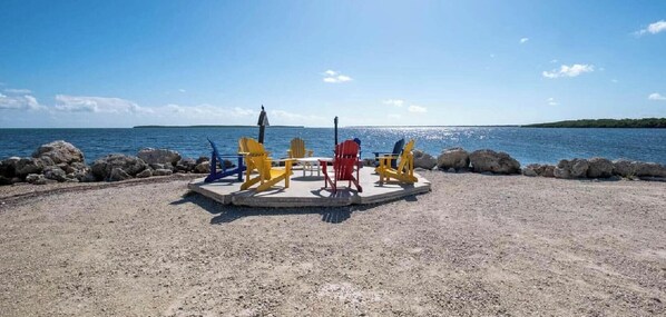 Une plage avec une zone de galets, une petite scène et des fauteuils Adirondack aux couleurs vives, ainsi qu’un rivage rocheux.