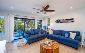 Ein modernes Wohnzimmer mit zwei Sofas, einem Couchtisch, einem Deckenventilator und einem großen Fenster mit Jalousien.