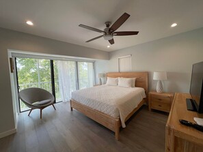 Une chambre à coucher comprenant un lit, une chaise, un bureau, un téléviseur et un ventilateur de plafond.