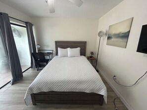 A bedroom with a large bed, a desk with a chair, a floor lamp, and a painting on the wall. - Lagoon View Free Kayaks Pool Playground Pickle Ball (Key Largo)